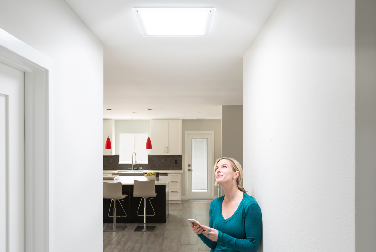 Woman standing in hallway looking up at natural light from Solatube skylight illuminating modern home interior